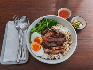 Dish of Thai stewed pork leg with boiled egg on rice or Kao Kha Moo in thai language in white plate on wooden table decoration background, selective focus point, top view.

