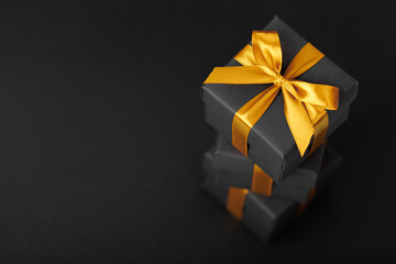 Black gift box with golden ribbon bow on black background