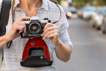 Retro film photo camera with a leather case in female hands on the city street. Woman photographer...