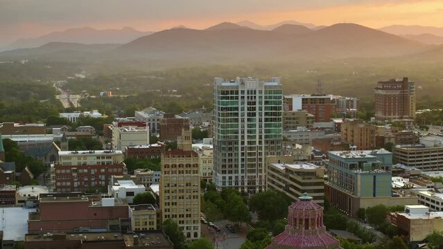Aerial view of Asheville city in North Carolina with high buildings and Appalachian mountain hills in distance at sunset. US travel destination