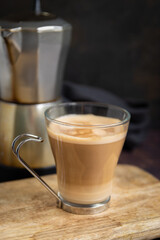 Cup of coffee with milk on wooden table and Italian coffee pot in the background. Vertical