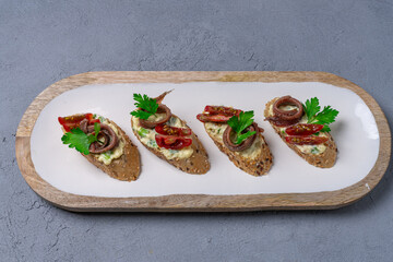 Sandwiches with anchovies and tomato on a white plate and on a concrete table. View from above.