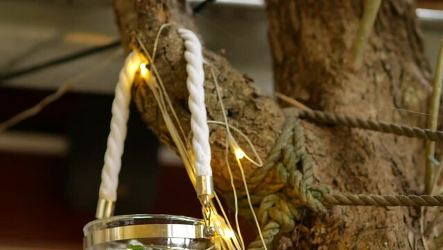 Glass jar with text quote Enjoy the Little Things hanging on a white rope on a tree branch. LED light garland. Halloween decoration to attract guests to restaurant. Rovinj, Croatia - November 14, 2023