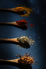 Several wooden spoons with spices, on a dark background.