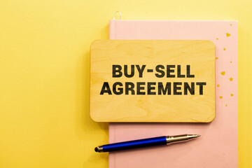 blank note pad with BUY-SELL AGREEMENT text on blue wooden background