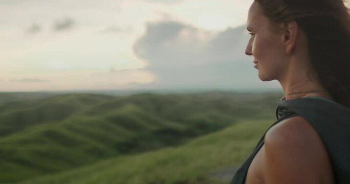 Brunette woman enjoy sunset green hill meadow landscape. Wind blow long hair. Great wild nature of Indonesia, Sumba. Girl having fun, relax, feel freedom. Outdoor travel. Zoom in portrait, slow motion