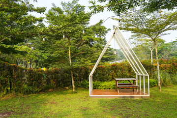 Fototapeta na wymiar Minimalist White glass canvas gazebo with wooden table chairs garden furniture on summer green lawn.