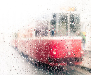 silhouette of a red tram seen from a rainy drop covered window