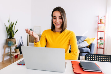 Portrait of pretty young woman having video call on laptop computer sitting on the table. Happy female working from home. Business and education concept.