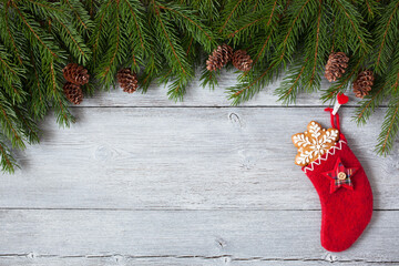 Christmas wooden background with fir branches, cones, red sock with gift, snowflake cookies. Copy space, congratulation text