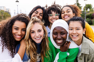 United portrait of young multiracial girls smiling at camera standing together outdoors. Millennial female friends feeling hugging each other smiling and posing for a photo. Women community concept. - obrazy, fototapety, plakaty