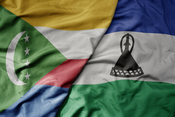 big waving national colorful flag of lesotho and national flag of comoros .