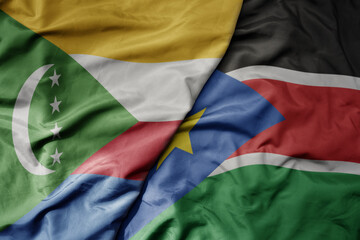 big waving national colorful flag of south sudan and national flag of comoros .