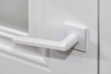 White door handle on a closed white interior door, close-up. Modern door fittings. Minimalism in...