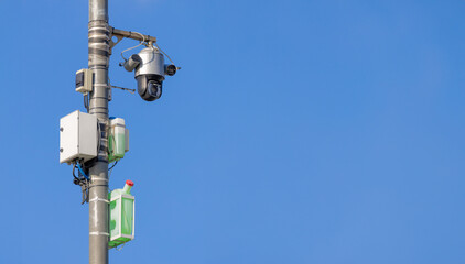 A road surveillance camera mounted on a high pole monitors the movement of vehicles. Nearby is a washer reservoir. Security and surveillance technologies in urban environments. Clear blue sky