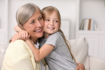 Happy grandmother hugging her granddaughter at home, space for text