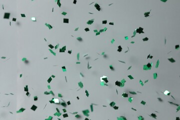Shiny green confetti falling down on light grey background