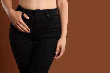 Woman wearing stylish black jeans on brown background, closeup. Space for text