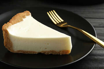 Piece of tasty vegan tofu cheesecake and fork on black wooden table, closeup