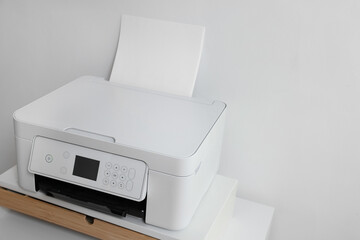 Modern printer with paper on table near white wall, space for text