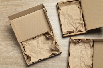 Open cardboard boxes with crumpled paper on wooden background, flat lay. Packaging goods