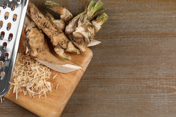 Grated horseradish and roots on wooden table, flat lay. Space for text