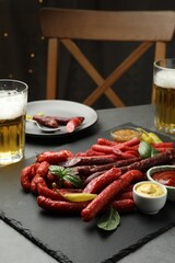 Different thin dry smoked sausages, sauces and glasses of beer on grey table