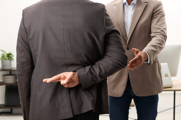 Employee crossing fingers behind his back while meeting with boss in office, closeup