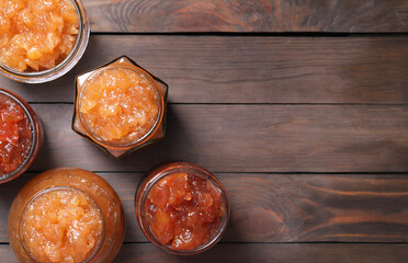 Delicious apple jam in jars on wooden table, flat lay. Space for text