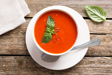 Delicious tomato soup with basil, spices and spoon on wooden table, flat lay