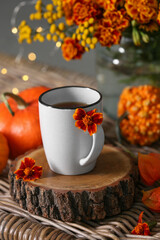 Beautiful autumn composition with cup of drink and flowers on wicker table