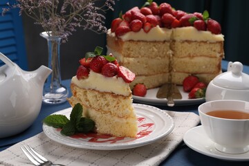 Piece of tasty cake with fresh strawberries, mint and cup of tea on blue wooden table