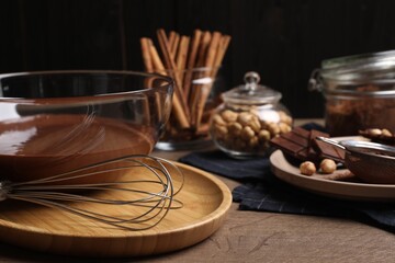 Bowl of chocolate cream with whisk and ingredients on wooden table