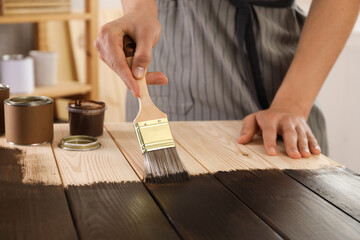 Fototapeta na wymiar Man with brush applying wood stain onto wooden surface indoors, closeup