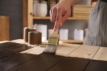 Man with brush applying wood stain onto wooden surface indoors, closeup