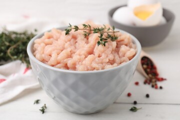Fototapeta na wymiar Fresh raw minced meat and thyme in bowl on white wooden table, closeup