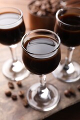 Shot glasses with coffee liqueur and beans on wooden table, closeup