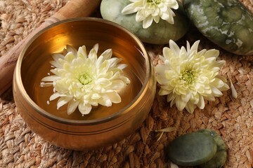 Tibetan singing bowl with water, beautiful chrysanthemum flowers, mallet and stones on table, closeup
