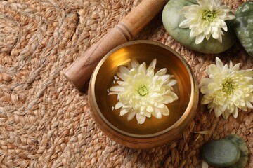 Fototapeta na wymiar Tibetan singing bowl with water, beautiful chrysanthemum flowers, mallet and stones on table, above view. Space for text