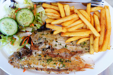 Close-up of a mouthwatering dish of golden fried potatoes, crispy fish fillet, and a side of vibrant green salad. The perfect combination of flavors and textures for a satisfying and wholesome meal.