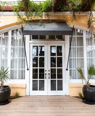 Front view of glass double doors surrounded by arched windows and beige stucco, green awning and hanging vines