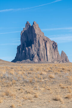 Shiprock in the four corners area of New Mexico on a sunny day with clear blue sky. The towering rock formation rises more than a thousand feet above the high desert plains.