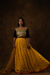girl wearing indian wear - black blouse and yellow lehenga and dupatta beautiful makeup holding flowers in her hand in black background