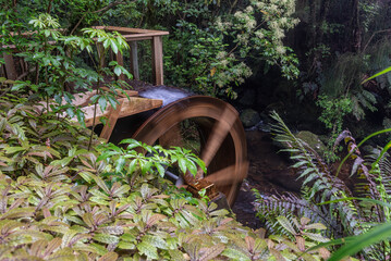 Small water wheel fed by a wooden chute in a forest setting.