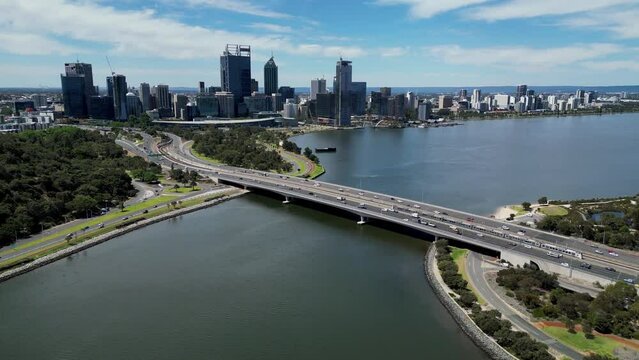 View by drone tracking towards Perth, Western Australia, flying over Narrows Bridge on the Swan River, train crossing the bridge between both lanes of traffic.