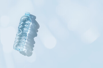 Plastic bottle water at sunlight with beautiful sun shadow on blue color background, copy space. Clean drinking water in bottle. Pollution, environment protection concept. World water problem
