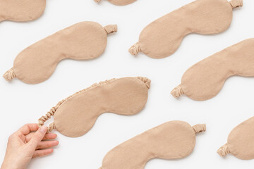 Creative minimal pattern from beige textile sleep masks on white light background. Woman hand take eye mask, comfort rest and quality sleep concept. Aesthetic top view composition