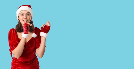 Young woman in Santa hat showing silence gesture on blue background with space for text