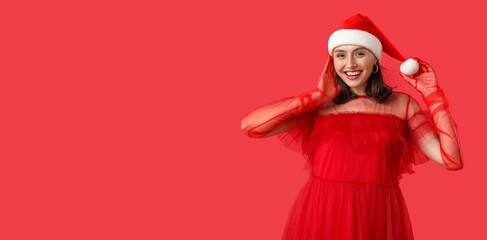 Fototapeta premium Happy young woman in Santa hat on red background with space for text