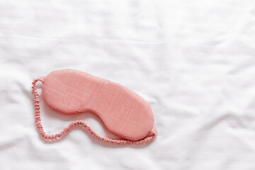Above view pink sleep mask on white wavy cloth background. Eye cover mask for best sleep. Concept of home comfort and wellbeing, dream well, comfort rest at night. Minimal Aesthetic style